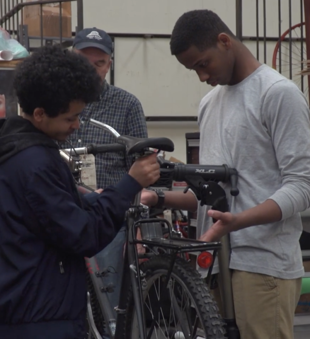 Two young men work together to fix a bicycle.