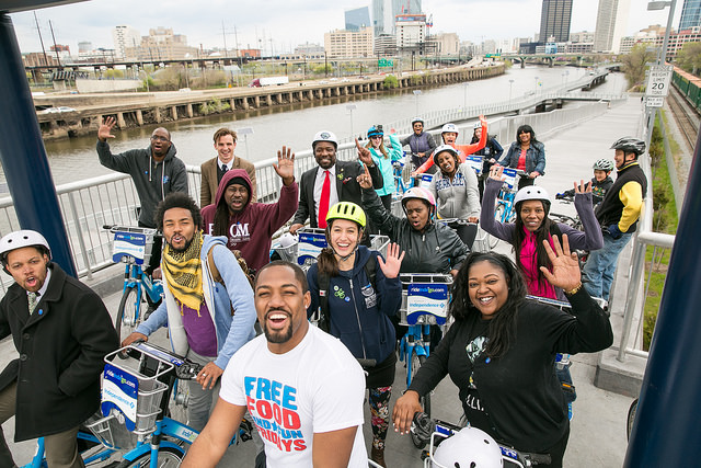 A group of people on Indego e-bikes smile and wave